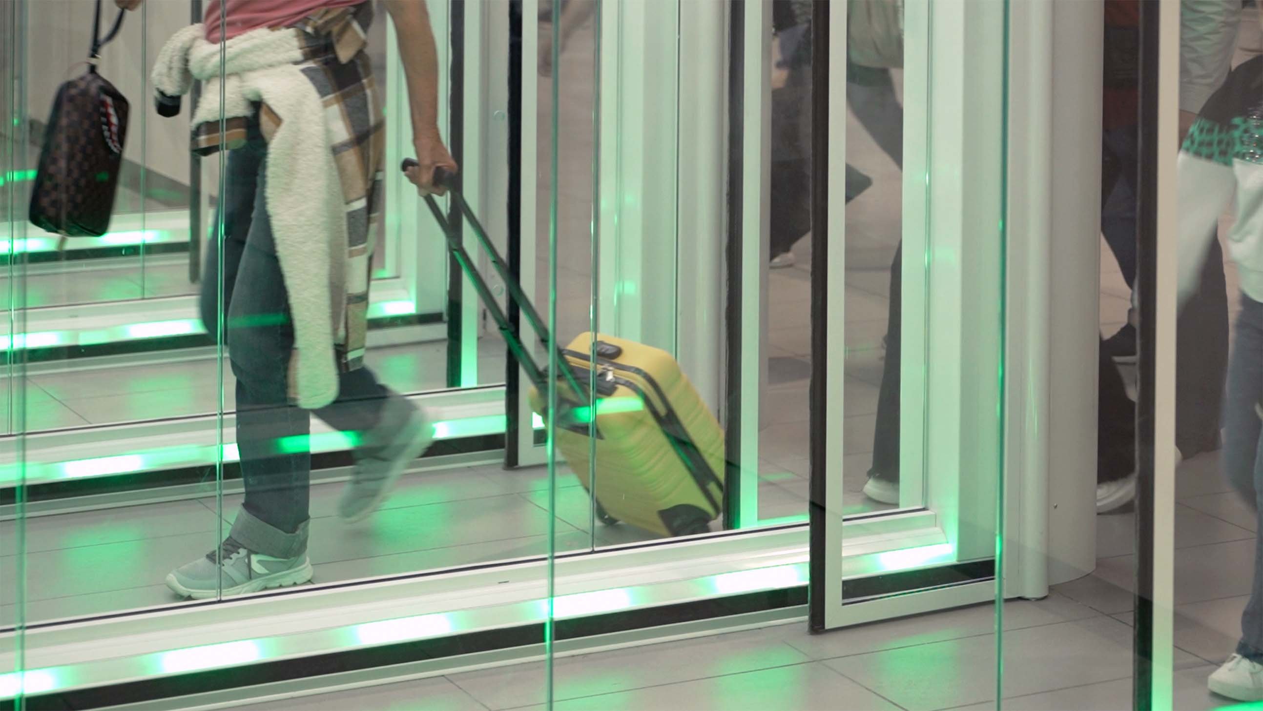 Passeggero con trolley attraversa un One-Way Corridor FAAC con segnalazione LED verde che indica il passaggio disponibile